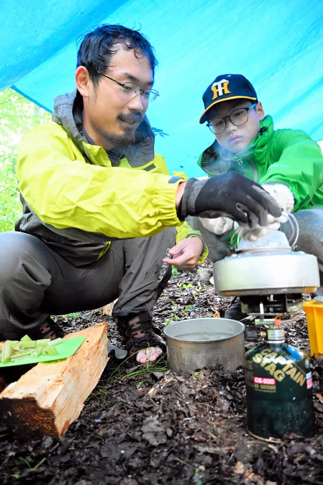 サバイバルキャンプで米を炊く平岡さん（右）。米は量が少ないのでおかゆにし、カジカの唐揚げなどを食べた
