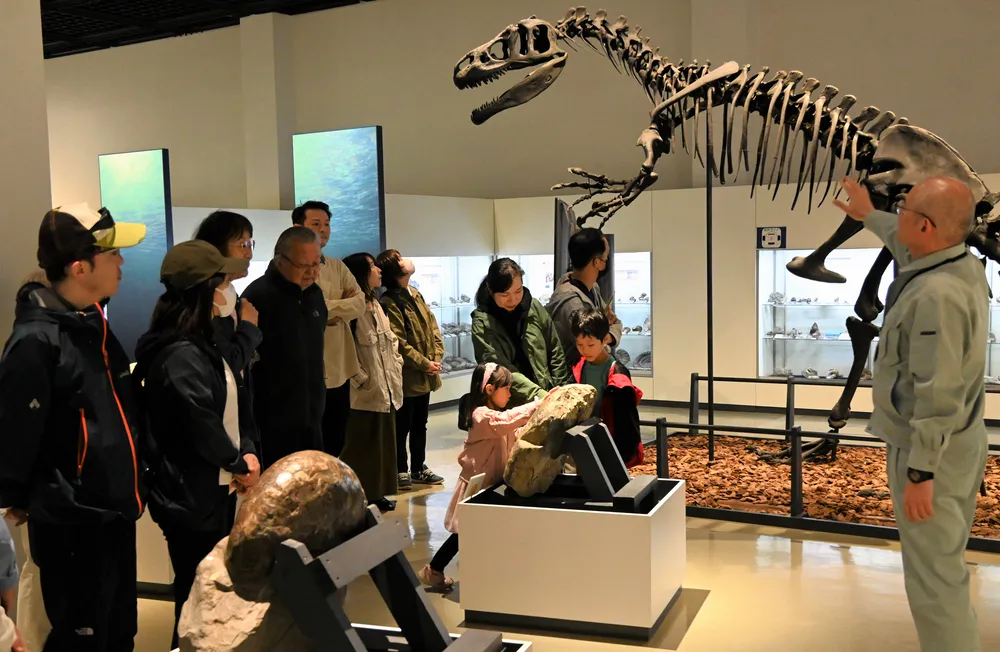 恐竜の骨格標本の解説をする加納館長（右）とツアーの参加者