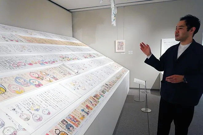 最長18メートルの障子紙の絵巻や絵はがきなどの鈴村さんの作品を前に「故郷から切り離されるのは痛いことなのだと感じる。帰れない深刻な状況下でどのような表現が紡がれたのか、見過ごしてはいけない」と話す国立ハンセン病資料館の吉国元学芸員