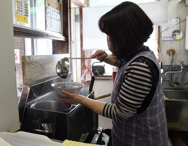 丼に手際よくそばつゆを注ぐ女性店員