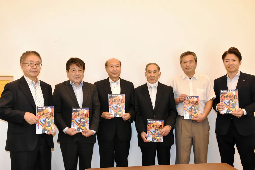 天狗の火渡りが紹介され、寄贈された「和祭巡礼画報」を手にする三浦教育長（左から3人目）ら