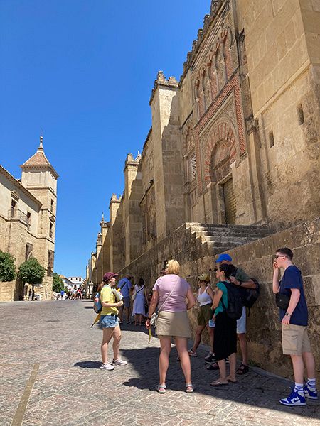 スペイン・コルドバの歴史地区で建物の日陰に入り、ガイドの説明を聞く観光客。空は抜けるように青い＝７月１日（内本智子撮影）