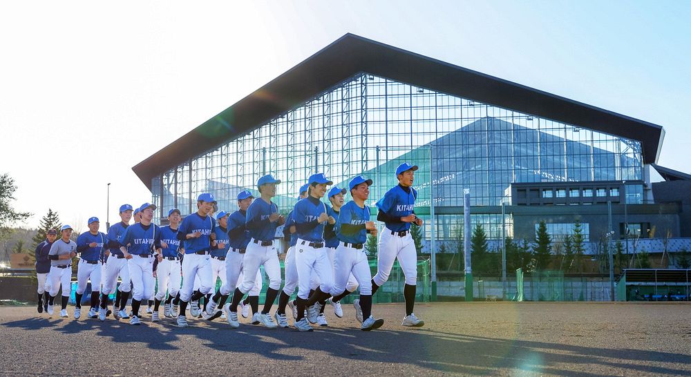 グラウンドでランニングをする北広島高野球部の部員たち。エスコンフィールド北海道に見守られるような場で日々練習に励んでいる（野沢俊介撮影） 