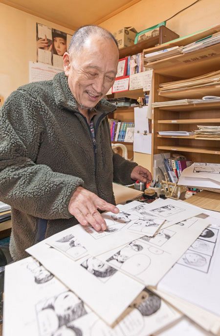 ６・５畳の仕事場で、漫画家デビューまでの道を振り返るハン角斉さん。手前はペン入れ前に繰り返し練習したキャラクターの絵