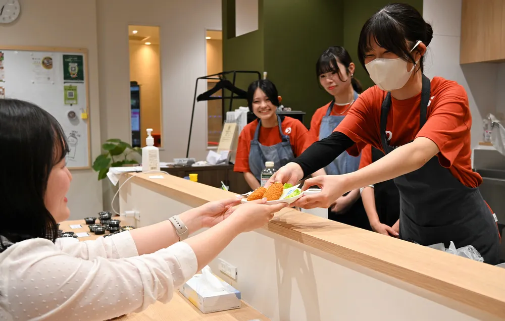 サンマルコ食品のコロッケを提供する札幌学院大学の学生（右）