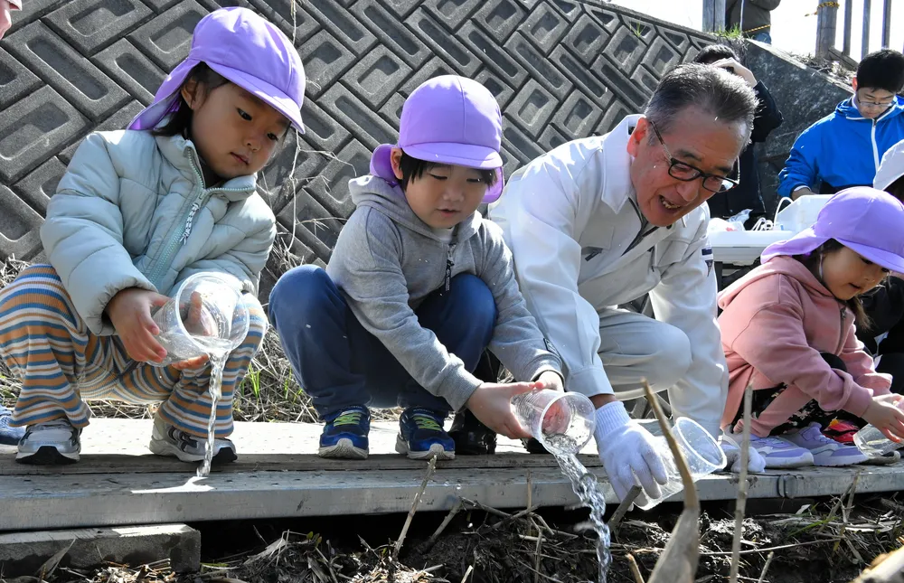 「元気でね」などと声をかけながら、稚魚を放流する西城賢策市長（左から3人目）と子どもたち