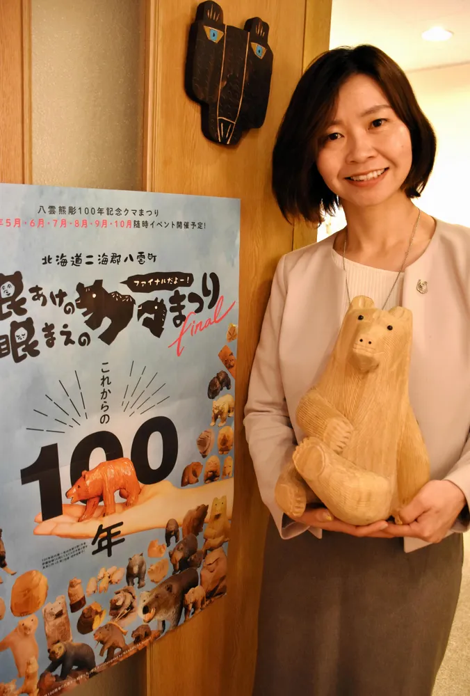 今年のクマまつりのポスターと青沼千鶴さん。手にしているのは増田皖應(きよたか)さんの木彫り熊