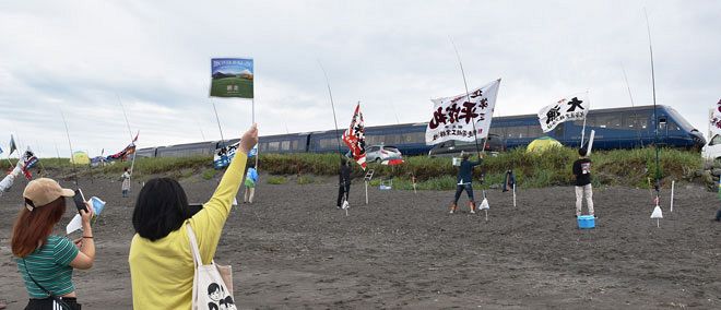 網走市の北浜海岸でザ・ロイヤルエクスプレスに小旗や大漁旗を振って歓迎する住民たち＝２０２２年８月（池野上遥撮影）