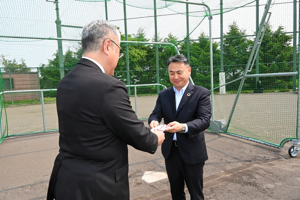 栗山高の坂上大介校長（左）にバッティングケージの目録を手渡す、わらべや日洋ホールディングスの辻英男社長