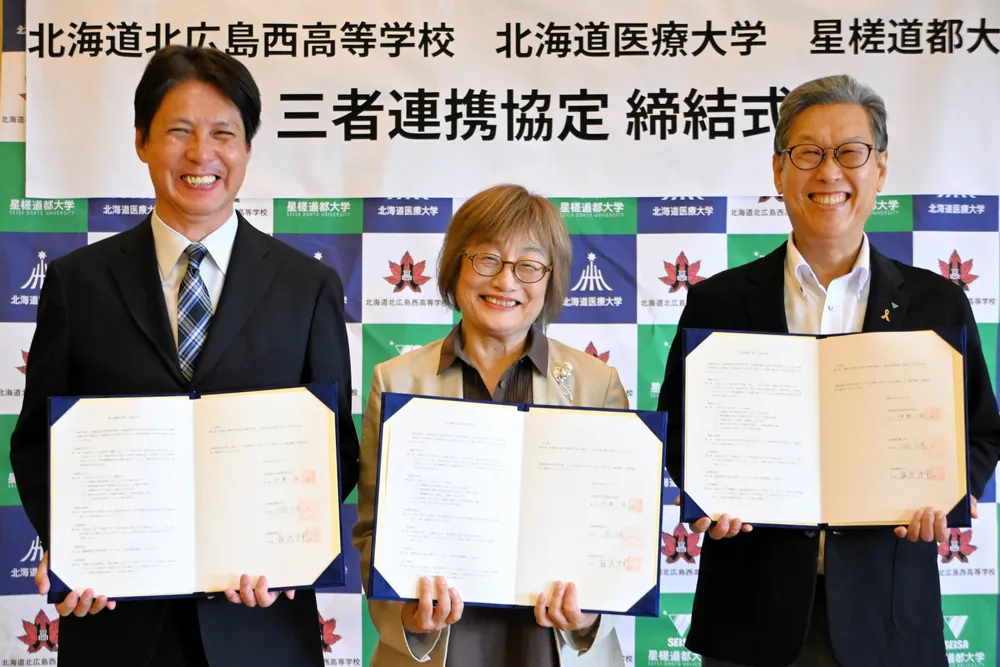 3者連携の協定書に署名し笑顔を見せる（左から）北広島西高の伊勢校長、道医療大の三国学長、星槎道都大の飯浜学長