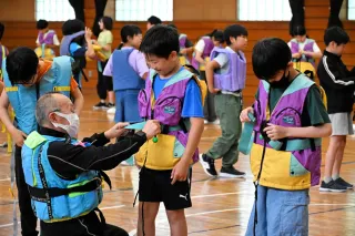 鳥畑博嗣さんから教わりながらライフジャケットを着用する児童