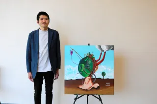 入選作品「自画像（アースマン）」の横に立つ岩原一さん