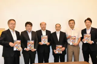 天狗の火渡りが紹介され、寄贈された「和祭巡礼画報」を手にする三浦教育長（左から3人目）ら