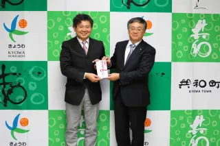 成田町長（右）に売り上げを手渡す石塚さん（町提供）