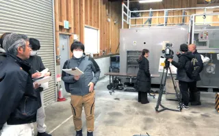 エゾシカやヒグマを微生物の働きで処理する減容化処理施設（奥の機器）。左は視察に訪れた南部桧山衛生処理組合の職員たち