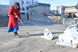 坂道にたまった大量の砂をほうきで集めて土のう袋に詰めるボランティアの藤間めぐみさん=3日